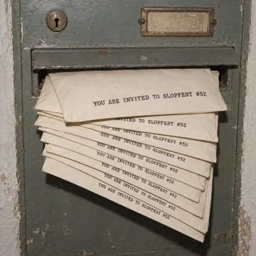 Close-up of a Viennese stairwell letterbox stuffed with 11 identical envelopes printed 'YOU ARE INVITED TO SLOPFEST #52'